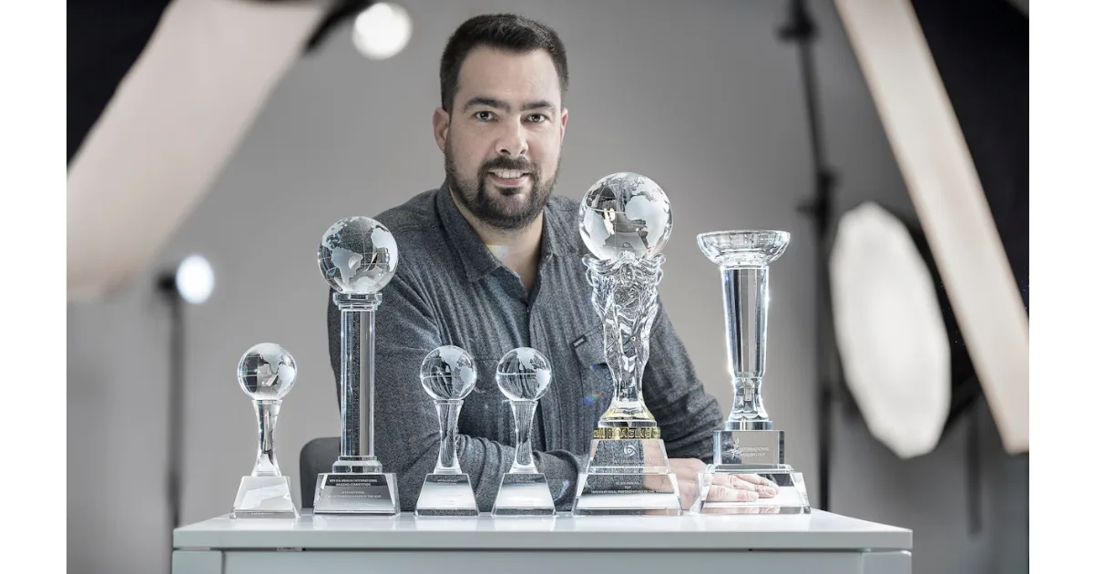 Homem com troféus de prêmios sobre a mesa.