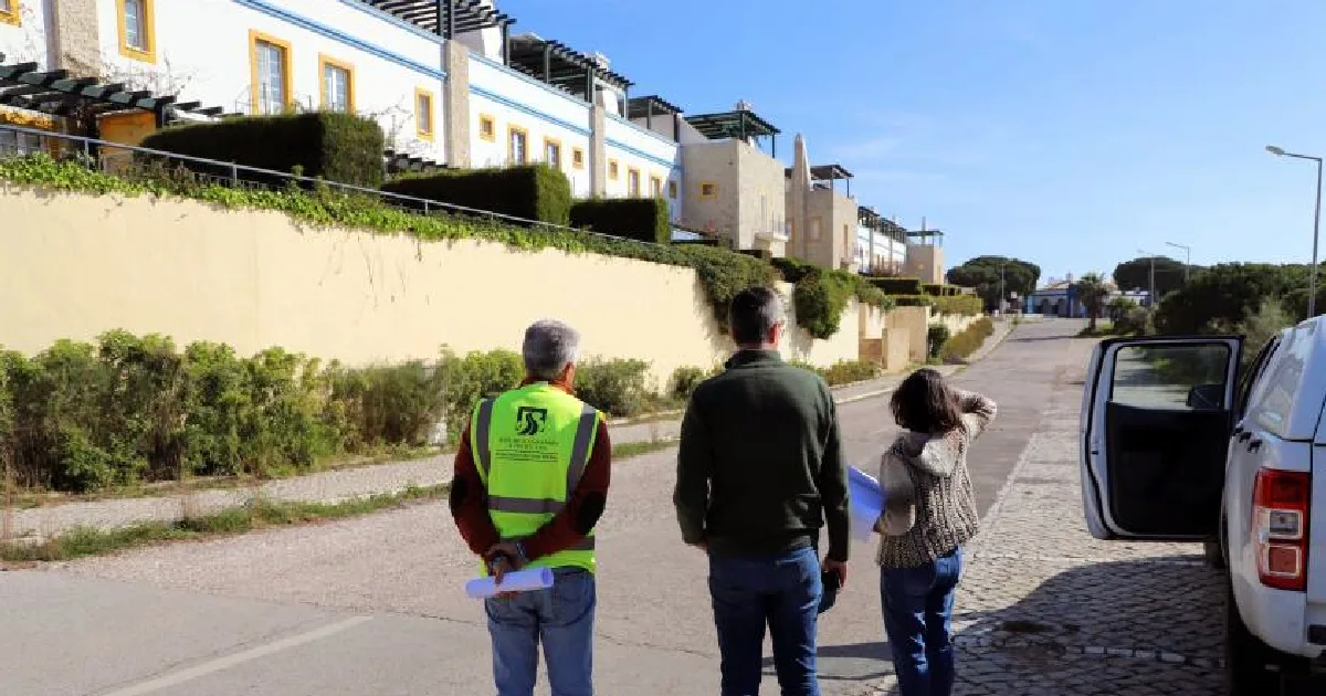 Três pessoas caminham em rua residencial ensolarada.