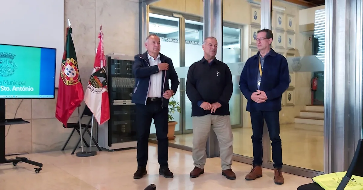 Três homens em evento municipal com bandeiras.