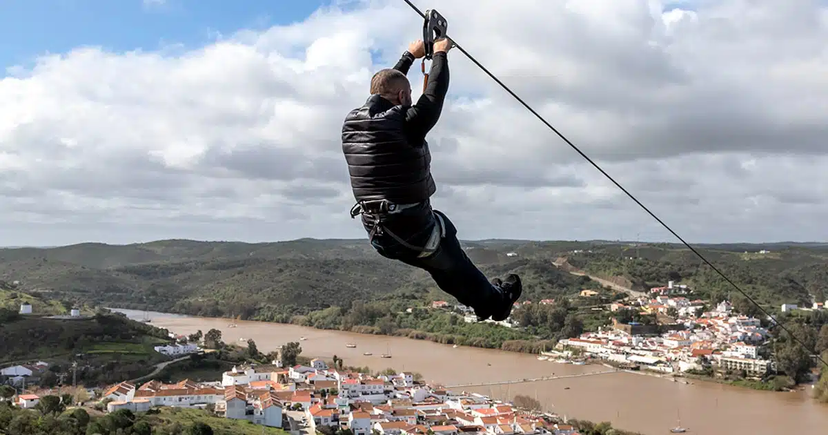 Homem praticando tirolesa sobre rio e cidade.