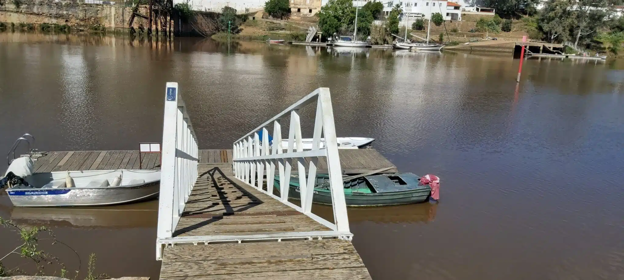 Doca fluvial com barcos e passadiço em madeira.